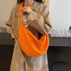 Large orange nylon dumpling crossbody bag worn by model in a stylish trench coat