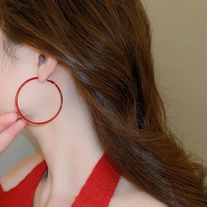 Macro view of minimalist large red hoop earrings with polished metal finish on model