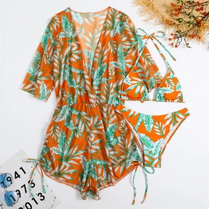 Detailed flat lay of tropical palm leaf print bikini set with orange mesh cover-up and accessories