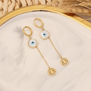 Gold tassel earrings with evil eye motif and shell disc on a marble display tray