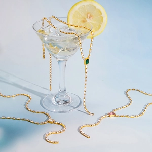 Elegantes collares tennis dorados con piedras esmeralda y rosa en una copa de martini