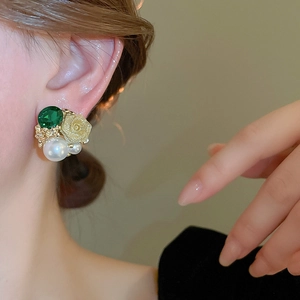 Gros plan de boucles d'oreilles avec pierre verte, perle blanche et fleur dorée