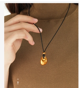 Close-up of a gold hollow water drop pendant necklace on a black cord worn by a model