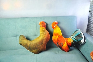 Detail of realistic rooster and hen plush pillows with feather print on a green sofa