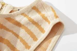 Dettaglio top in maglia a righe beige e gialle con chiusura a zip dorata lucida