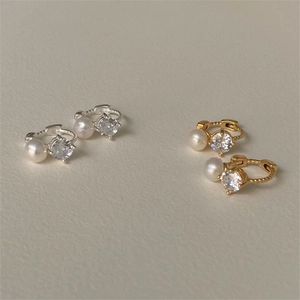 Macro shot of gold and silver huggie earrings with white pearls and bright zircon stones