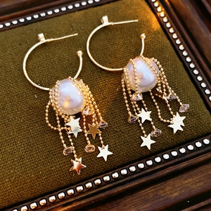 Détail de boucles d'oreilles pompons étoiles et perles sur fond de velours vert