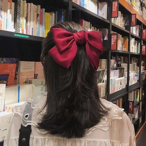 Close-up of a large wine red satin bow hair clip worn on the back of the head