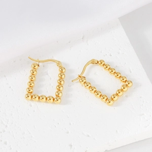 Close-up of golden geometric beaded earrings on white stone and silk fabric