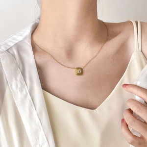 Detail of a gold choker featuring a geometric rectangular zircon pendant on a model