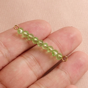 Detail of green crystal beads with gold metal loops on a minimalist jewelry piece