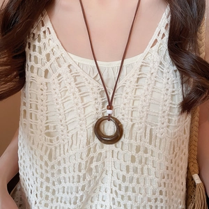 Detail shot of amber resin circle pendant on slim brown cord with lace clothing