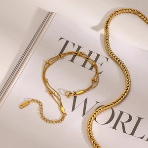 Detail of layered gold stainless steel bracelets and woven necklace on editorial background