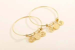 Detailed shot of adjustable gold zodiac bangles with Cancer and Scorpio pendants