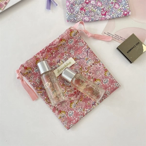 Pochette à cordon fleurie avec flacons de voyage disposés sur un fond blanc épuré