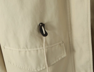 Detail of drawstring toggles and brown leather accents on khaki trench coat fabric