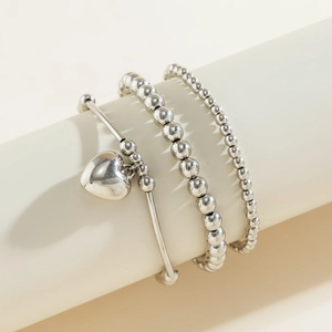 Stack of three silver metal bracelets featuring heart charm and beaded link designs