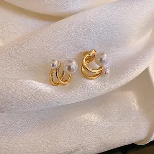 Minimalist C-shaped gold pearl earrings with double layer metal curves on silk background
