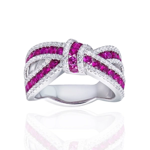 Detailed shot of bow-shaped ring with red gemstones and white diamonds on white reflection