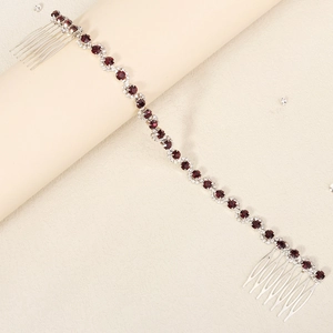 Detailed close-up of bridal hair comb chain with deep red crystals on a beige surface