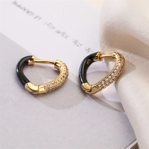 Close-up of gold heart earrings with black inlay and sparkling clear crystals on silk