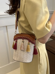 Detail of woven bucket bag with brown leather trim, colorful fringe and tassel accents