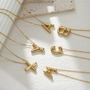 3D chunky gold initial letter necklaces with a glossy metallic finish on stone display