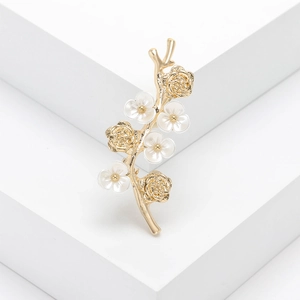 Elegant gold flower branch brooch with white mother of pearl petals on a white geometric stand