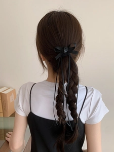 Vue détaillée d'une pince nœud en ruban noir avec rose sur des tresses arrière