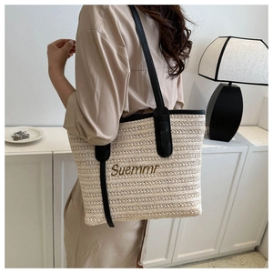 Detail of straw tote bag featuring black shoulder straps and golden Suemmr embroidery
