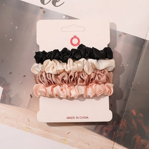 Detail view of 4-pack satin scrunchies in black, cream, gold, and pink on card