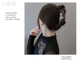 Detailed back view of a silver angel-shaped hair claw clip with rhinestones on black hair