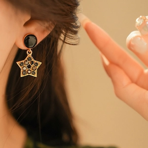 Gros plan de boucles d'oreilles étoile en émail noir et incrustation dorée sur modèle