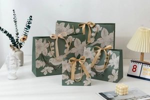 Detailed set of four green paper gift bags with bird motifs and golden ribbon handles