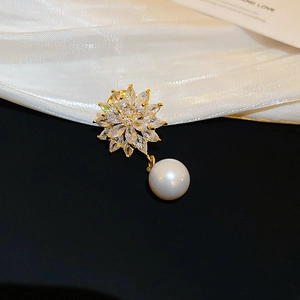 Close-up of gold-plated flower brooch with shimmering crystals and a lustrous pearl drop