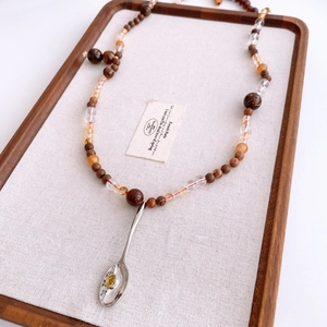 Détail du collier de perles en bois avec pendentif cuillère argentée et gemme jaune
