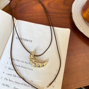 Detailed macro view of the golden croissant pendant on a minimalist brown cord necklace