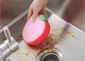 Close-up of apple-shaped sponge cleaning a stainless steel sink surface