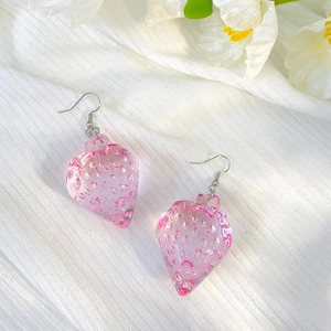 Detail of pink resin strawberry earrings with silver hooks on white textured fabric