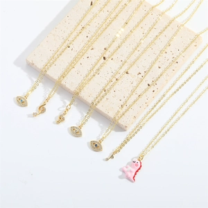 Detail of gold chain necklaces with blue evil eye, music note, and pink dinosaur charms