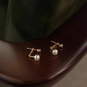 Close-up of J-shaped gold freshwater pearl earrings on dark wood and velvet
