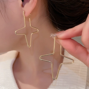 Detail of gold geometric cross star earrings shown on model with polished metal finish