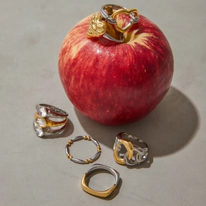 Macro shot of gold and silver heart zircon rings stacked on a red apple surface