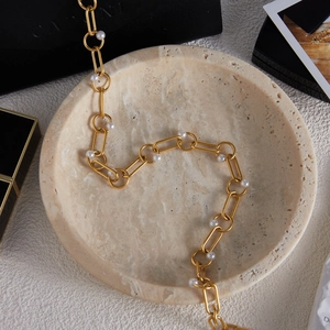 Macro detail of 18K gold-plated stainless steel chain necklace with pearls on a stone tray