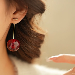 Macro close-up of a model wearing cherry earrings with red resin and gold flakes
