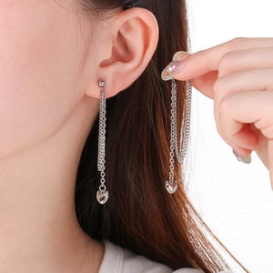 Detail of silver long chain earrings with heart pendants worn on a model's ear