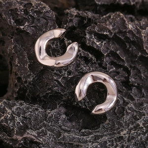 Macro detail of polished silver C-shaped thick ear cuffs on a dark mineral stone base