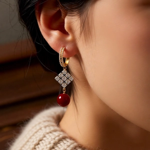 Détail de boucles d'oreilles dorées 18k avec perle rouge sur un modèle élégant