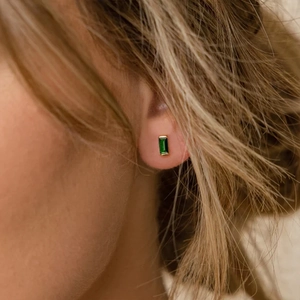 Close-up of gold-plated square stud earrings featuring deep green emerald-style zircons