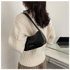 Model wearing a black glossy leather underarm bag over a beige knit sweater